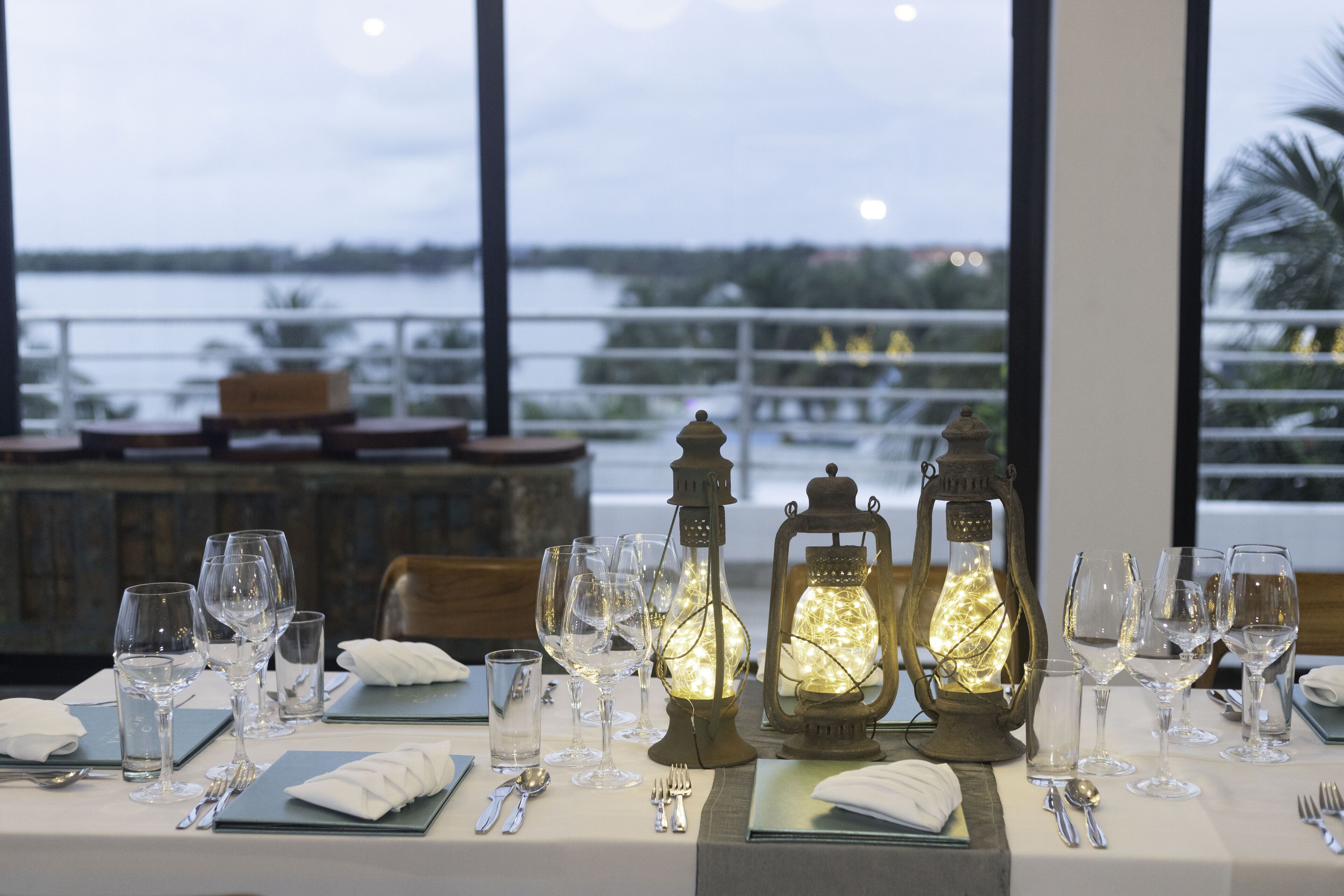 A dining table set for a meal with wine glasses, plates, and cutlery, overlooking a body of water.