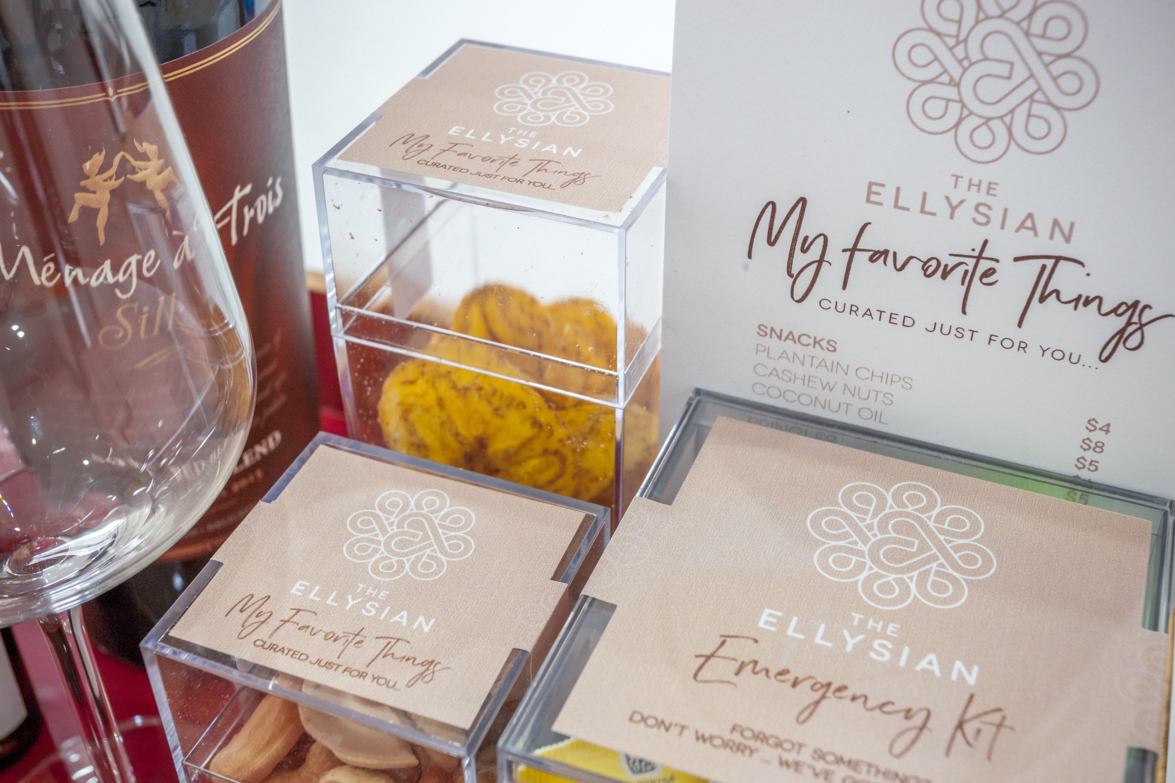 Eine Produktpräsentation mit Schildern, die "The Ellysian My Favorite Things" und "The Ellysian Emergency Kit" zeigen, darunter Snacks und weitere Artikel.