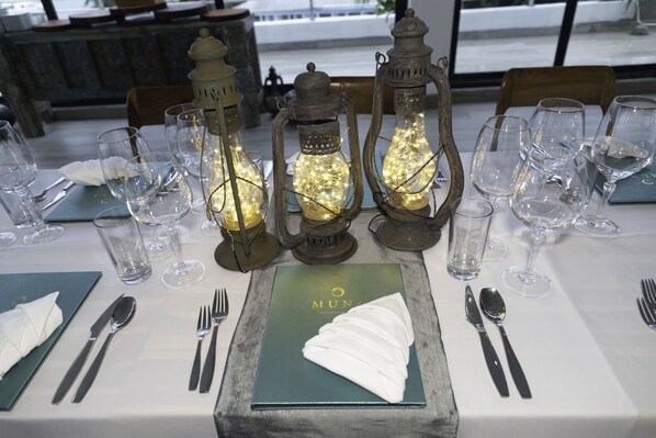 Mesa lista para comer, con copas de vino vacías, un mantel doblado y un menú con el título "MUNA".
