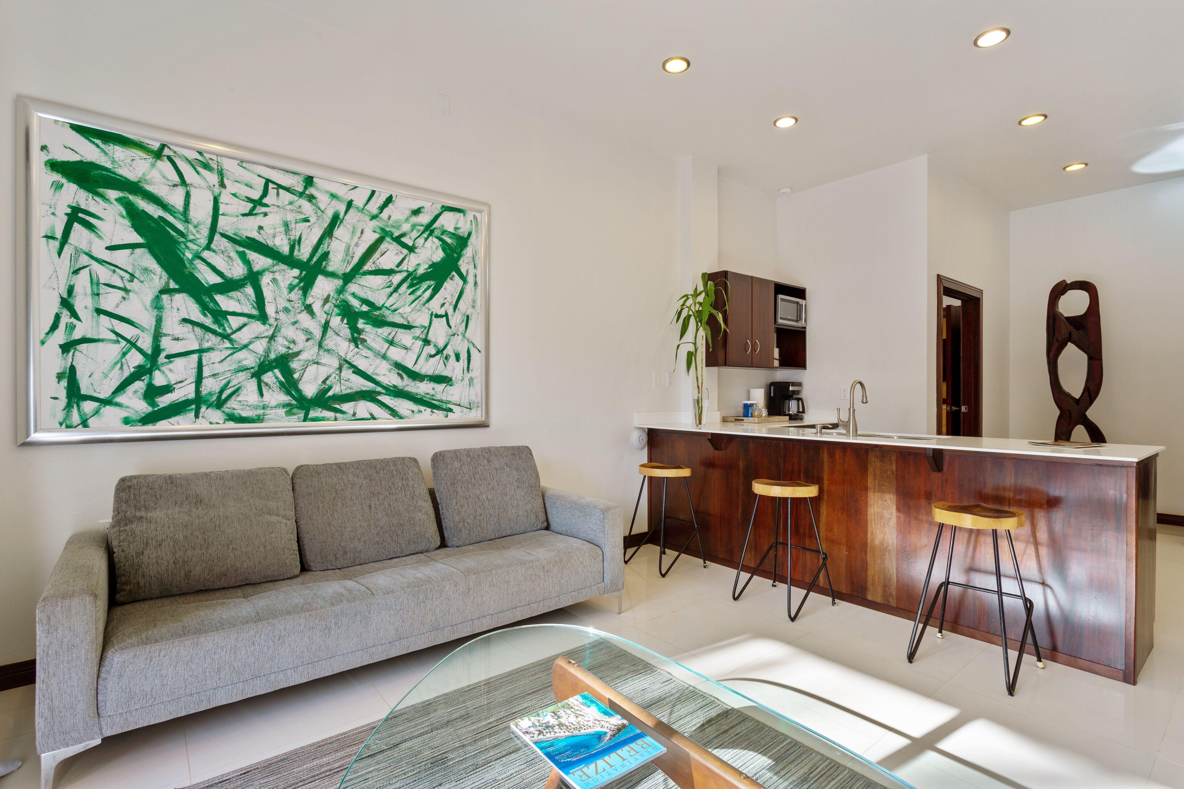 A modern living room with a grey sofa, a glass coffee table, and a large abstract painting on the wall.