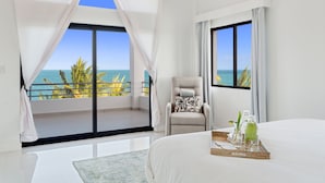 Un dormitorio con una cama grande, una silla, una bandeja con botellas y vistas al océano.