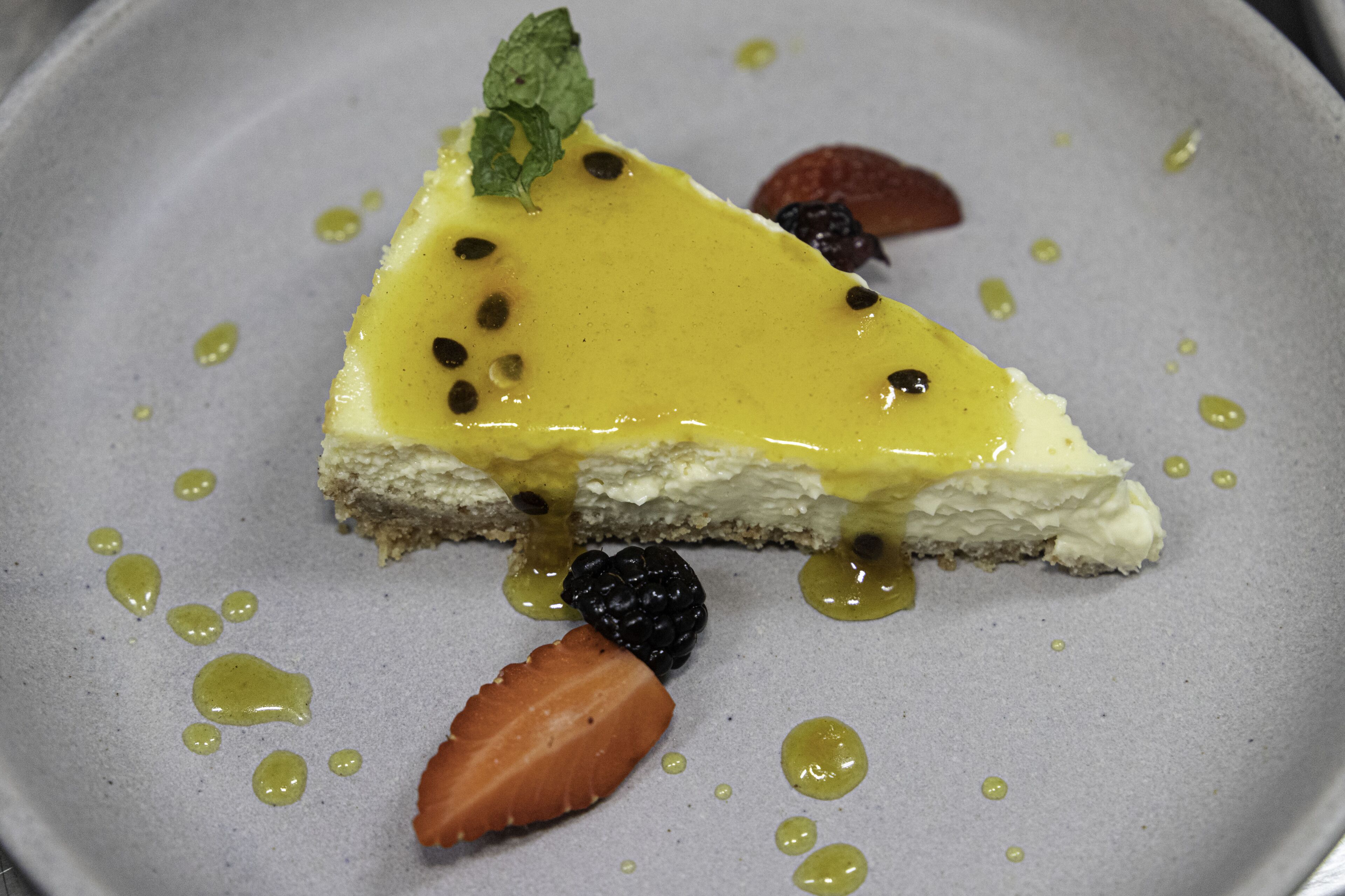 A slice of cheesecake with a yellow topping and berries on a plate.