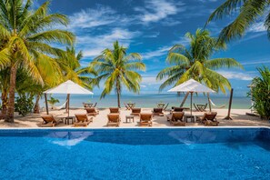 A pool area with lounge chairs and umbrellas, surrounded by palm trees and a view of the ocean. - The Ellysian Boutique Hotel (Placencia)
