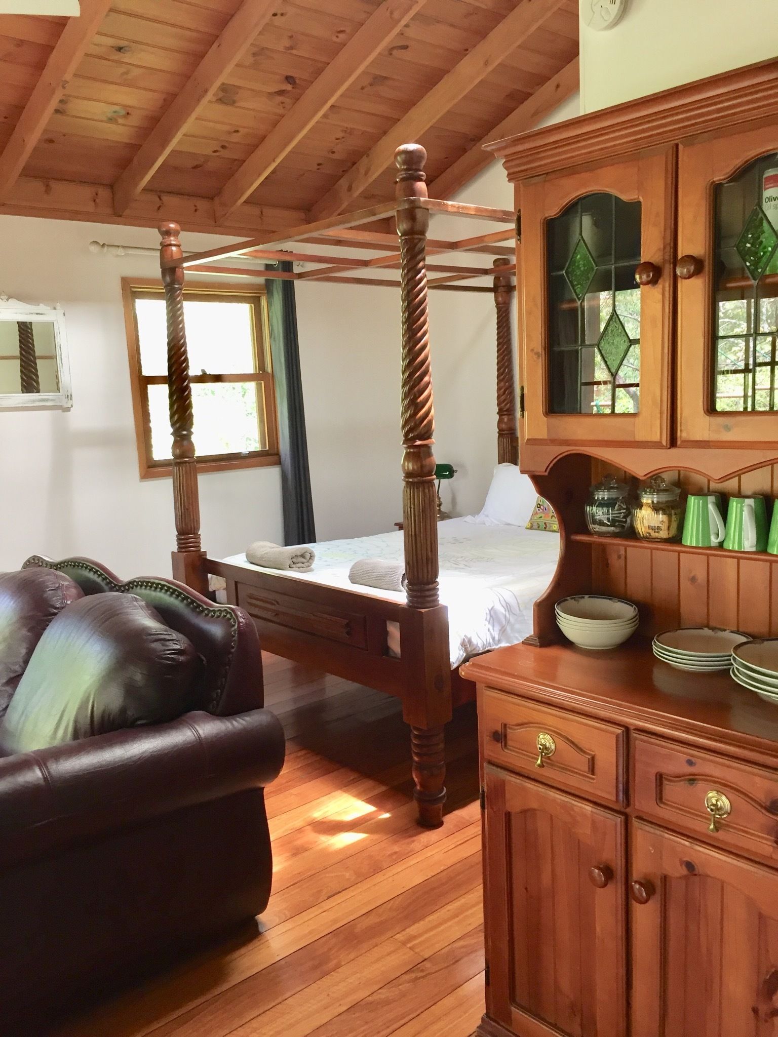 Una cama tradicional con dosel y un cabecero de madera, un sofá de cuero y un aparador con cajones.
