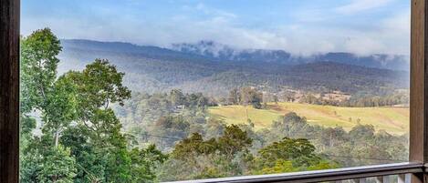 A view from a balcony overlooking a hilly landscape with trees and a distant mountain range.