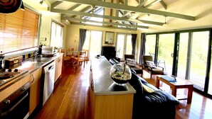 A spacious kitchen with wooden cabinets, a dining area with a glass-top table, and large windows offering a view of the outdoors.