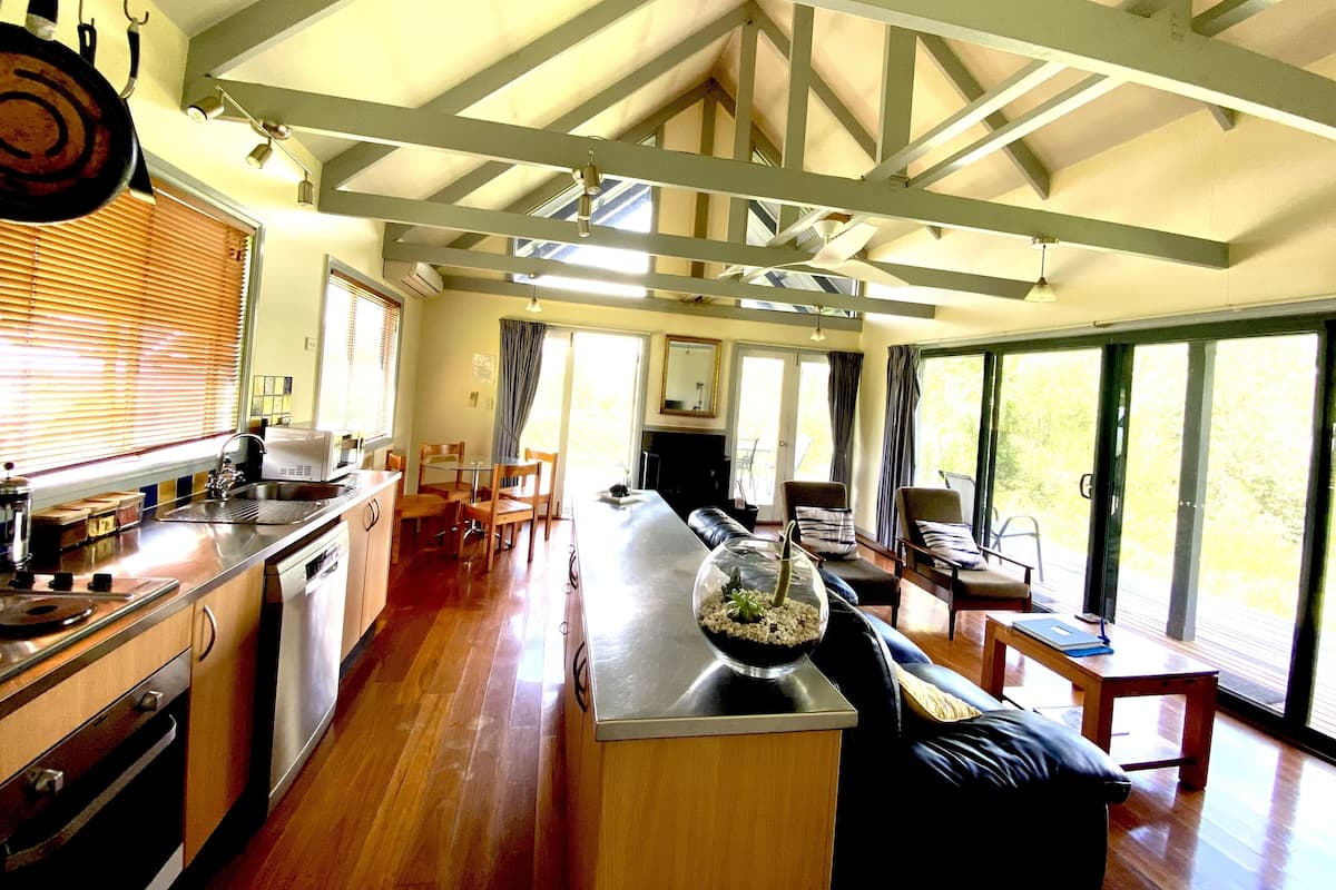 A spacious kitchen with wooden cabinets, a dining area with a glass-top table, and large windows offering a view of the outdoors.