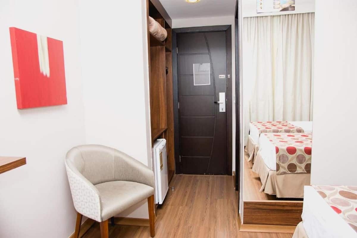 Una habitación de hotel con una cama, una silla, una puerta y una mesita.