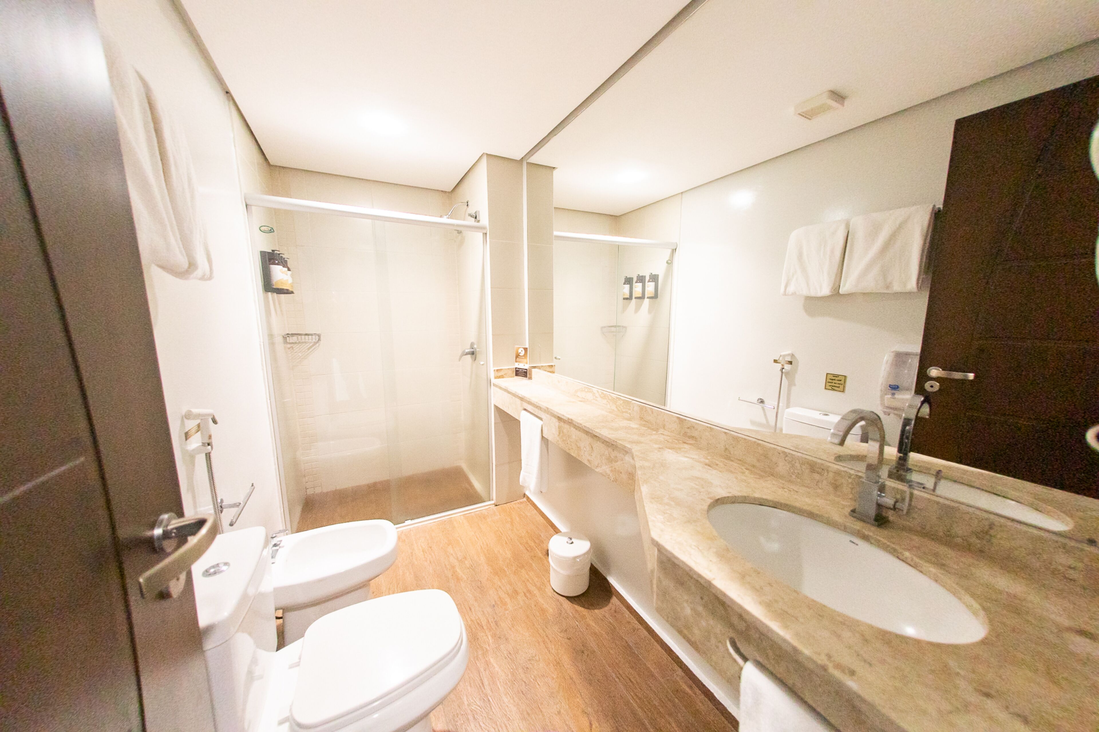 Ein modernes Badezimmer mit Dusche, zwei Toiletten, einem Waschbecken und einem großen Spiegel.