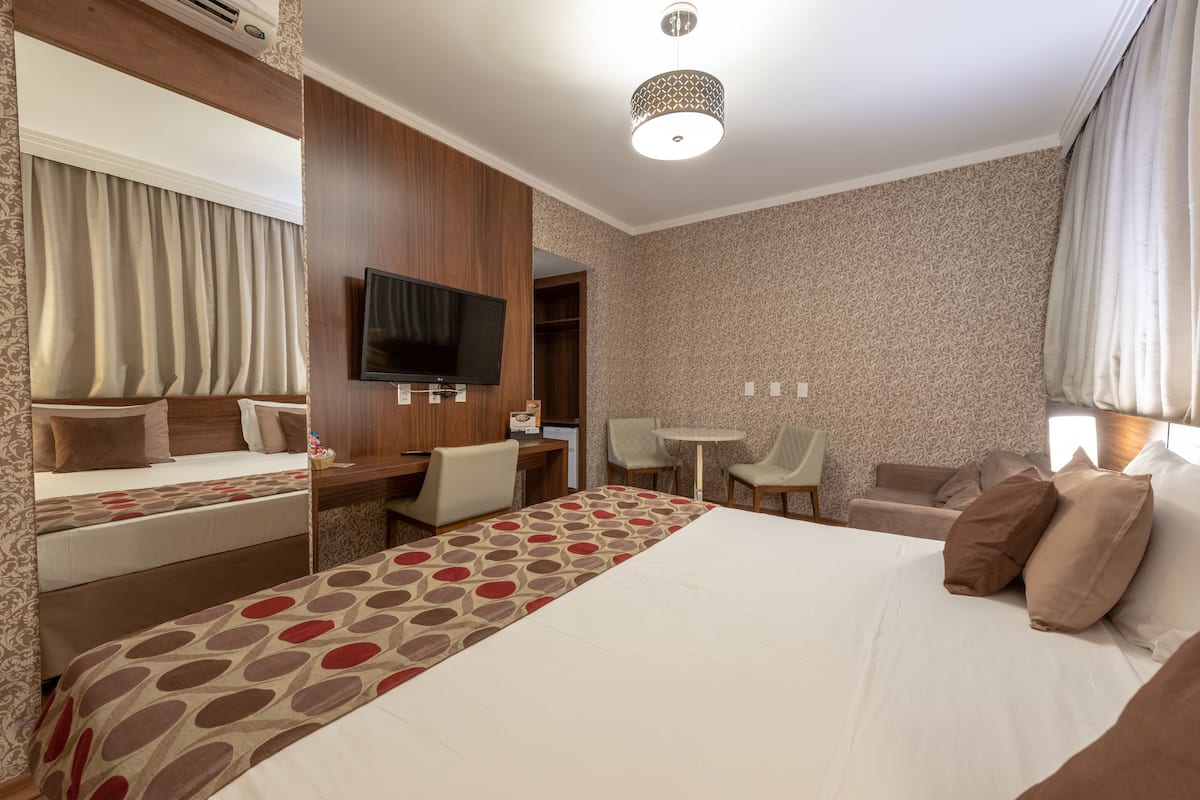 Habitación de hotel con una cama grande, un escritorio, un televisor, una mesita y un sofá.