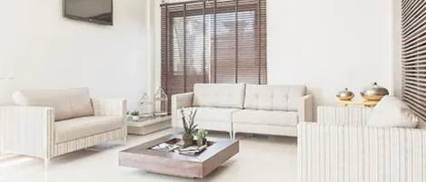 Una sala de estar moderna con un sofá, sillones, una mesa de centro y un televisor montado en la pared.