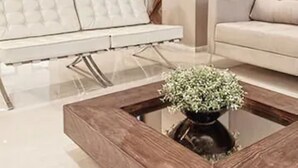 Een moderne woonkamer met een glazen salontafel, een bank en een televisie aan de muur.