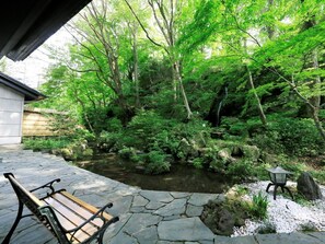 Ein Steinweg führt zu einem kleinen Teich, der von üppigem Grün und einer hölzernen Bank umgeben ist.