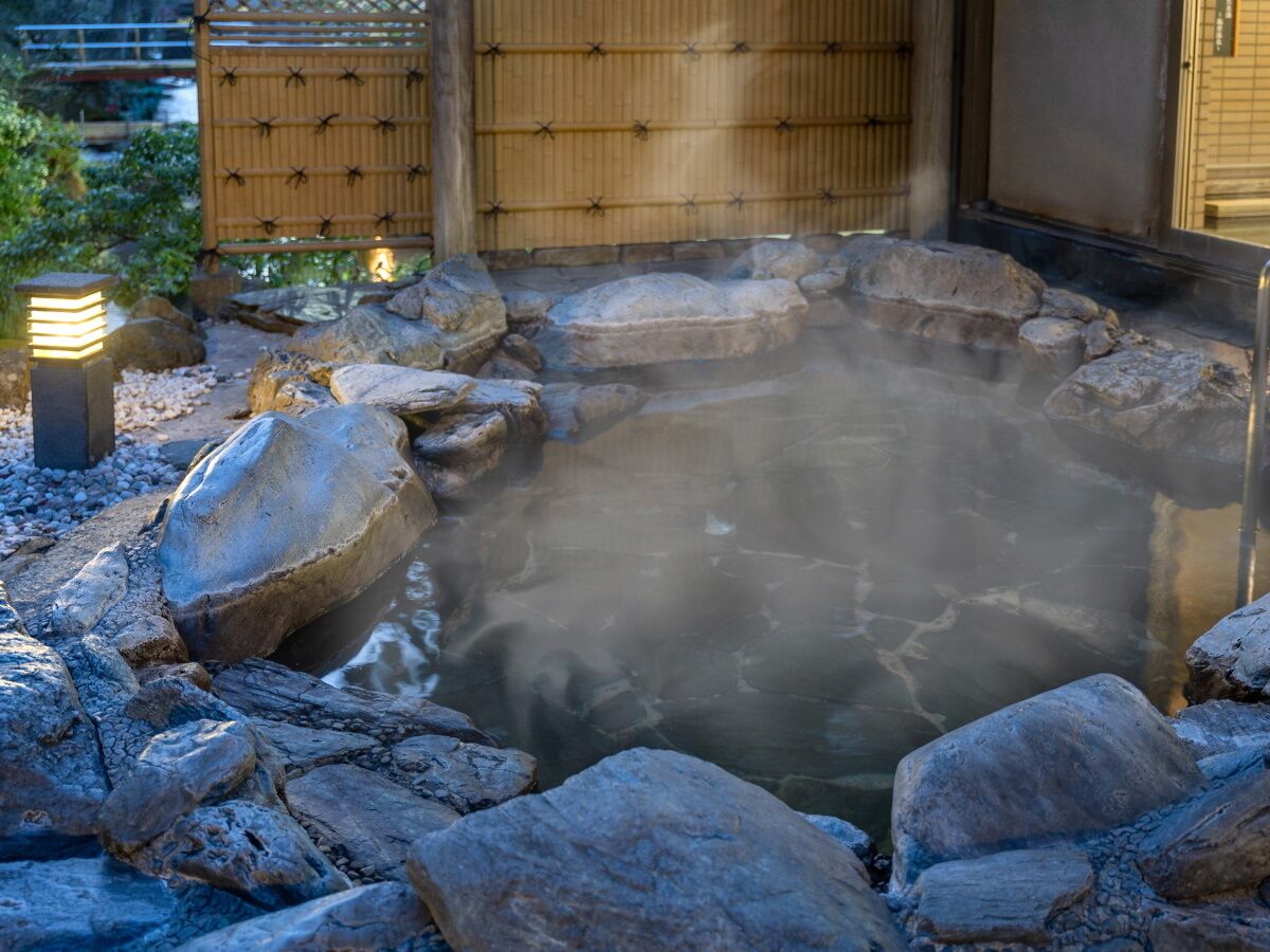 A hot spring surrounded by rocks and a bamboo fence.