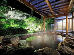 Un onsen japonais traditionnel, avec une structure en bois, un bain en pierre entouré de rochers et un décor luxuriant de verdure.