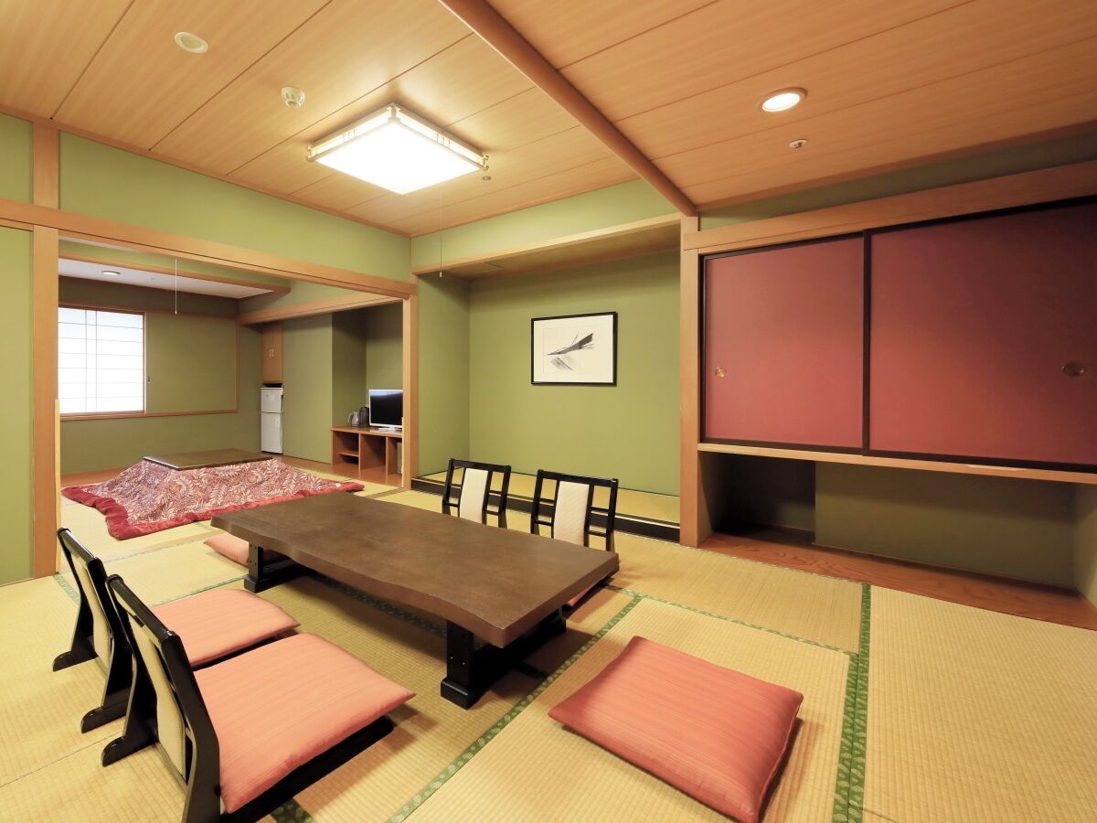 Ein Zimmer mit Tatami-Böden, einem niedrigen Tisch, Kissen und einem Futon.