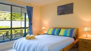 A bedroom with a large window, a bed with colorful pillows, two bedside lamps, and a painting on the wall. - Springview (Hepburn Springs)