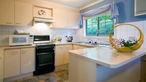 A kitchen with white cabinets, a stove, a microwave, a sink, and a window with a view of greenery. - Springview (Hepburn Springs)
