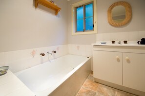 A bathroom with a bathtub, a window, a mirror, and a cabinet. - Springview (Hepburn Springs)