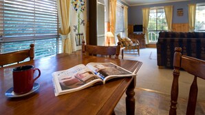 A wooden dining table with a magazine, a red cup, and a lamp in a cozy living room with a sofa and chairs. - Springview (Hepburn Springs)