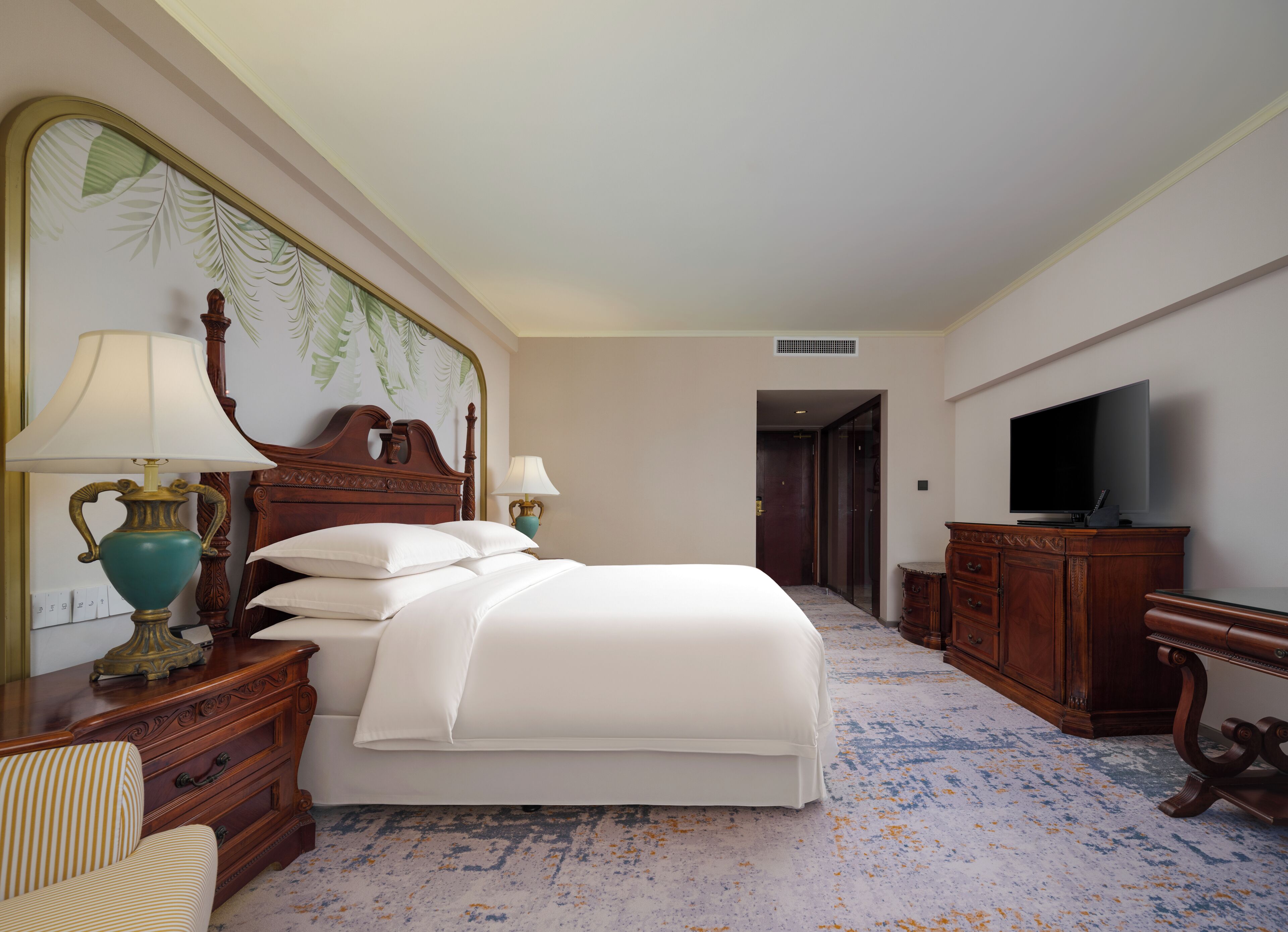 A hotel room with a large bed, two bedside tables with lamps, a television, and a wooden dresser.