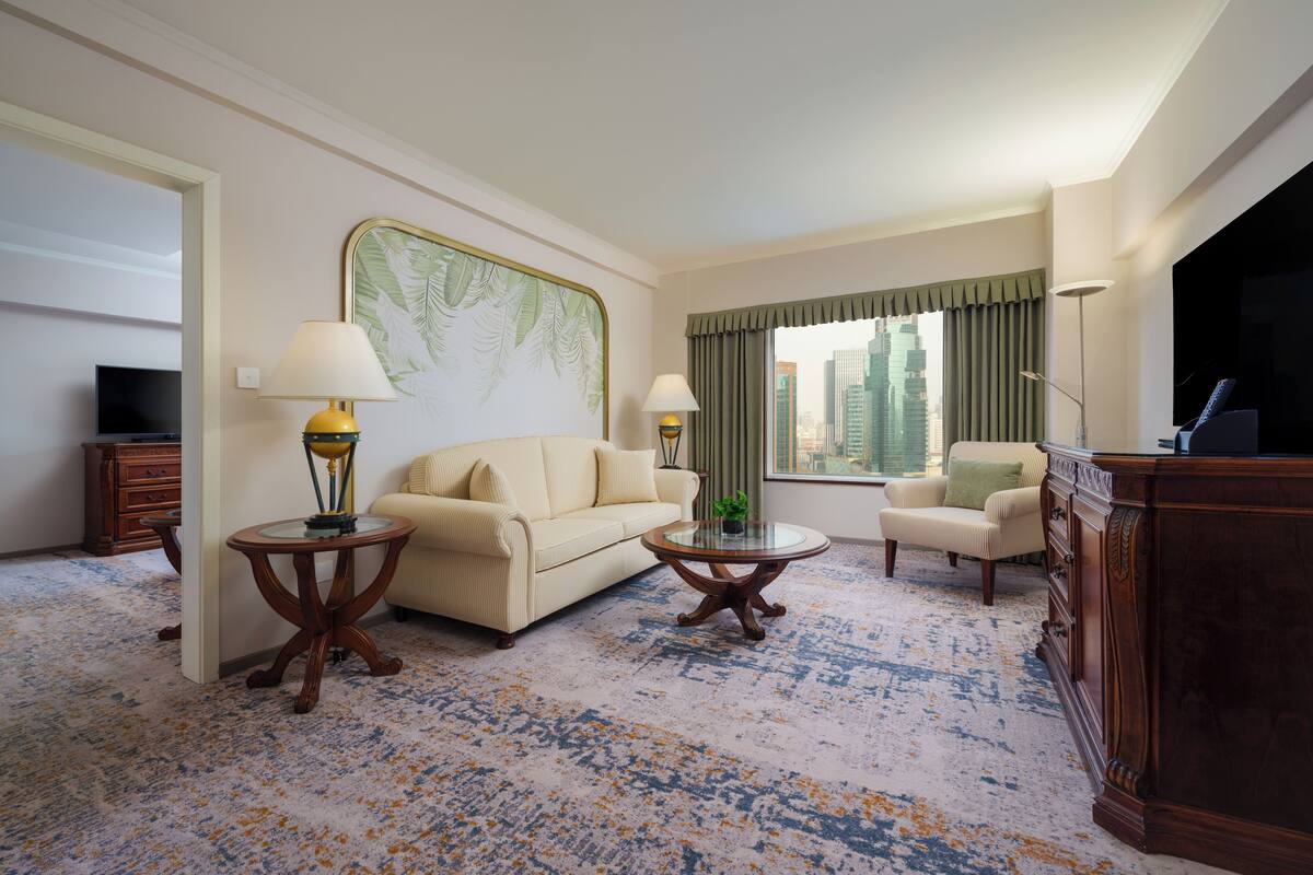 Quarto de hotel com sofá, poltrona, mesa de centro redonda e televisão.