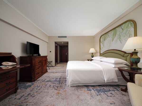 A hotel room with a bed, a television, a desk with a telephone, and a painting on the wall.