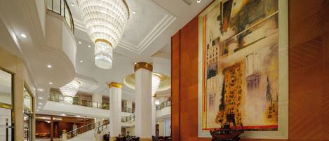 A spacious lobby with a grand chandelier, a large abstract painting, and a staircase leading to an upper level.