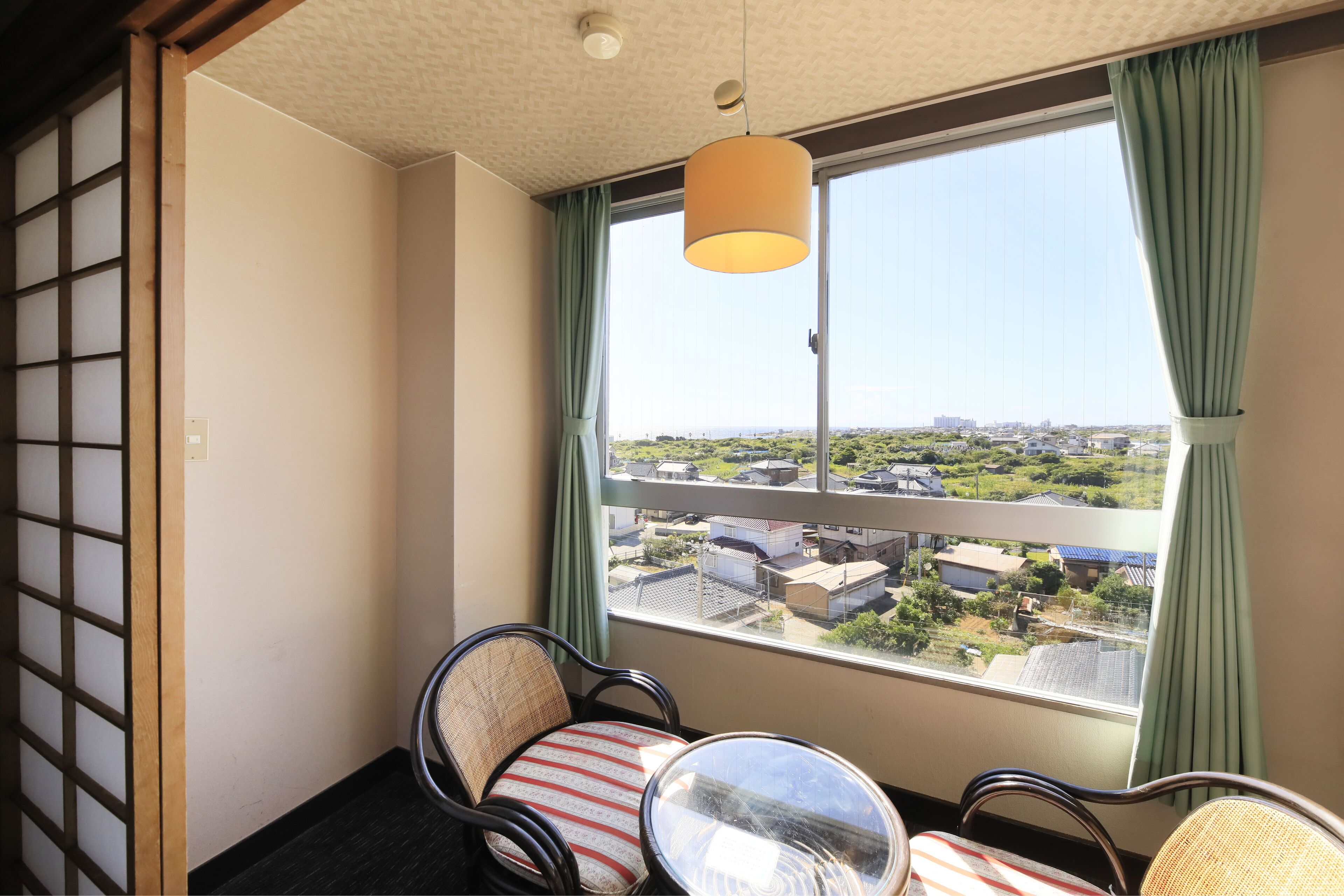 A room with a view of a residential area, a sliding door, and two chairs with cushions.