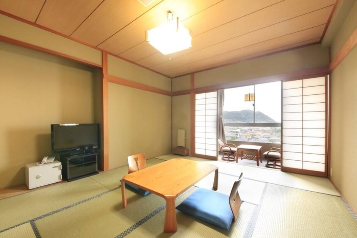 A traditional Japanese room with tatami flooring, a wooden table, a television, and a view of a mountain.
