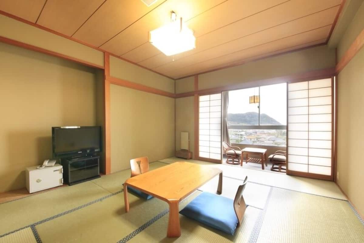 A traditional Japanese room with tatami flooring, a wooden table, a television, and a view of a mountain.