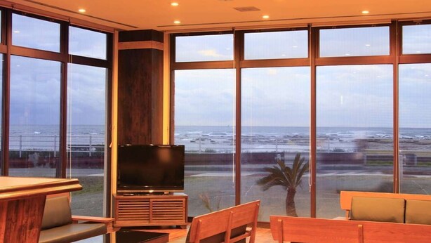 A modern living room with a large TV, wooden furniture, and a view of the ocean. - Bousou Shirahama Umisato Hotel (Minamiboso)