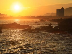 A sunset over a rocky coastline with buildings in the background. - Bousou Shirahama Umisato Hotel (Minamiboso)