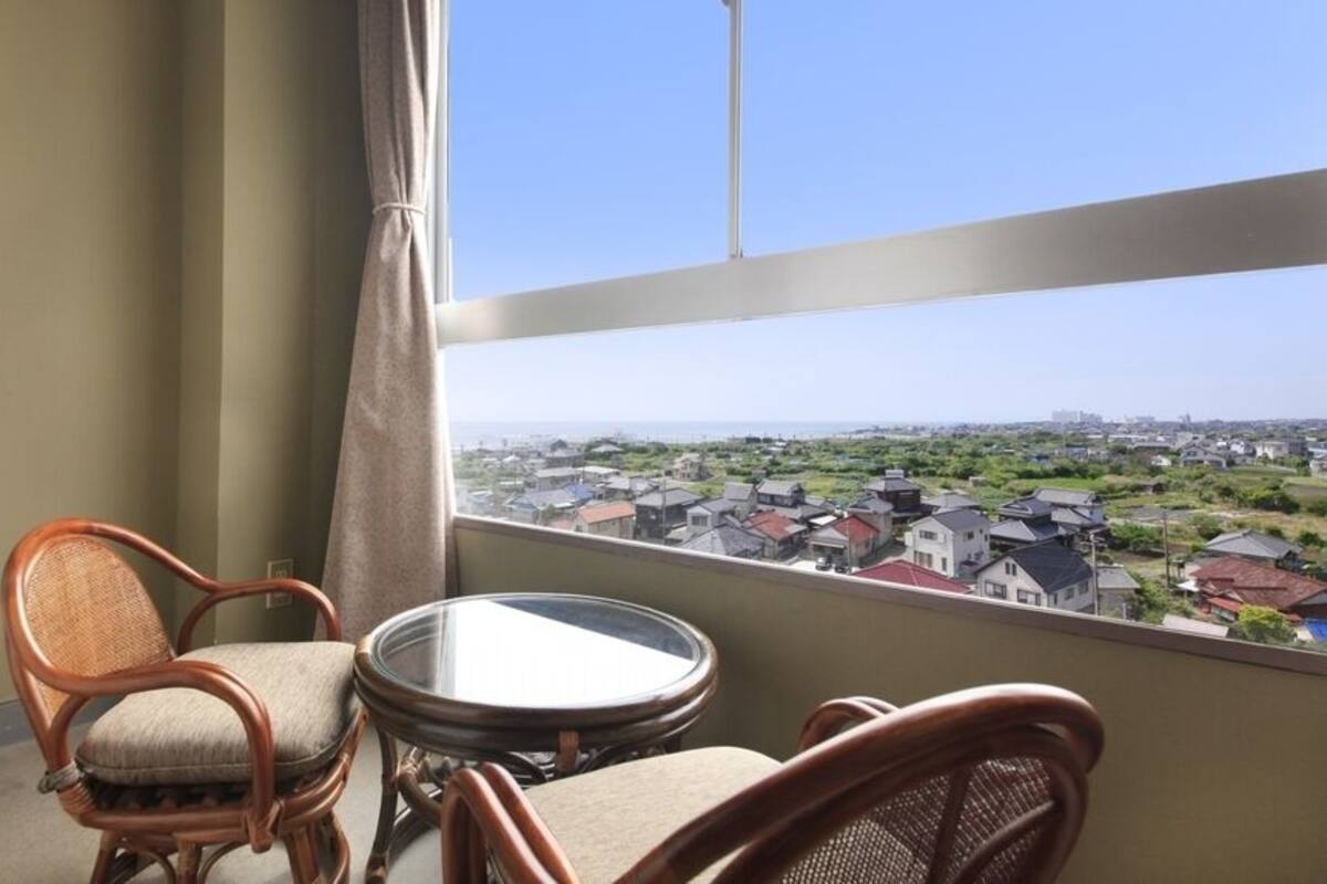 A balcony with wicker chairs and a small table, overlooking a residential area.