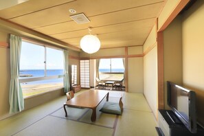A traditional Japanese room with tatami flooring, a low table, a television, and large windows overlooking a beach. - Bousou Shirahama Umisato Hotel (Minamiboso)