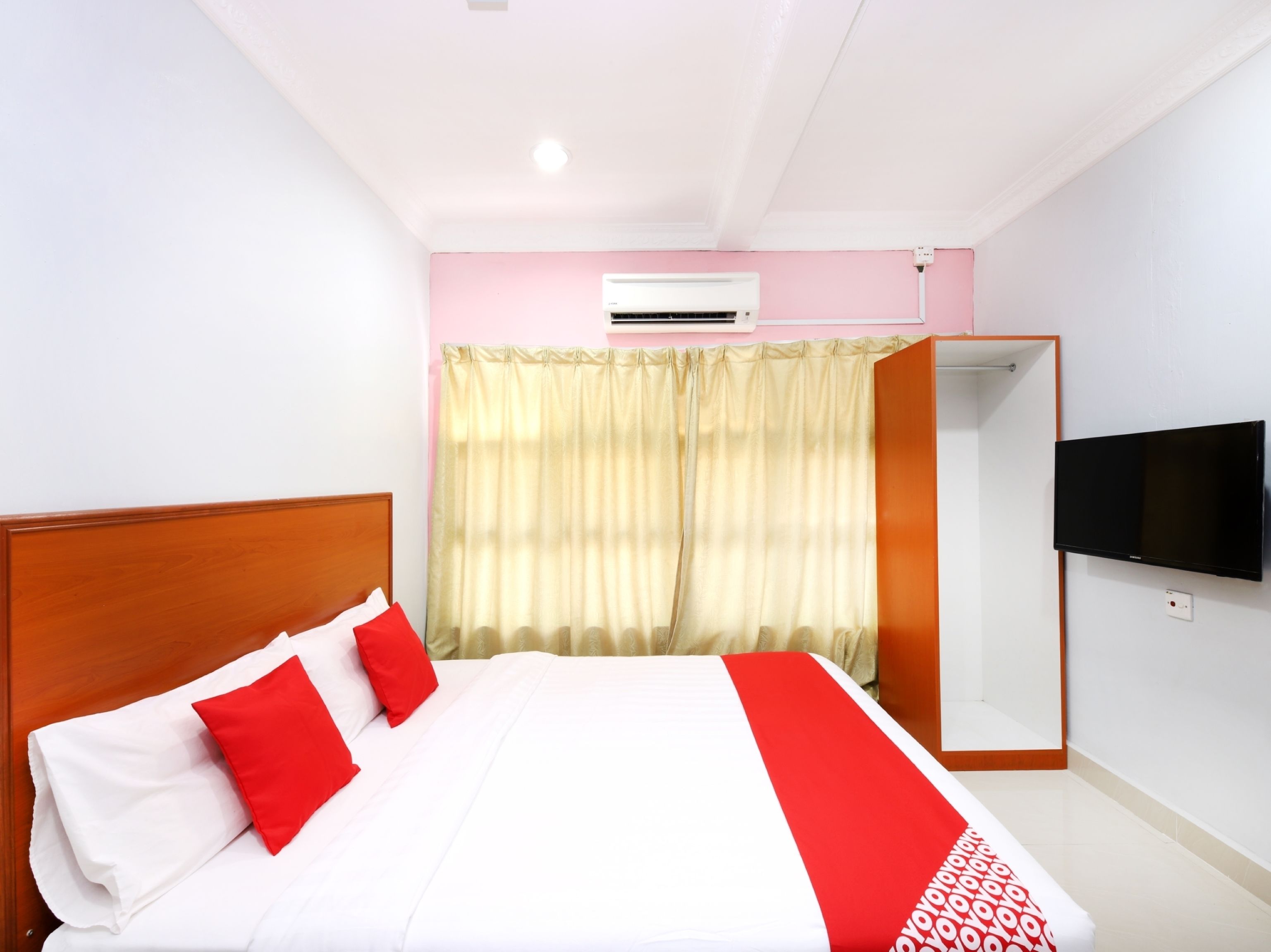 A hotel room with a bed, a TV mounted on the wall, and an air conditioning unit.