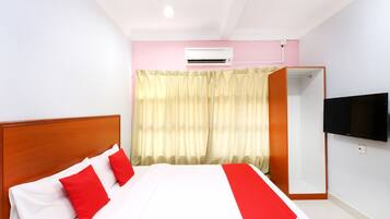 A hotel room with a bed, a TV mounted on the wall, and an air conditioning unit.