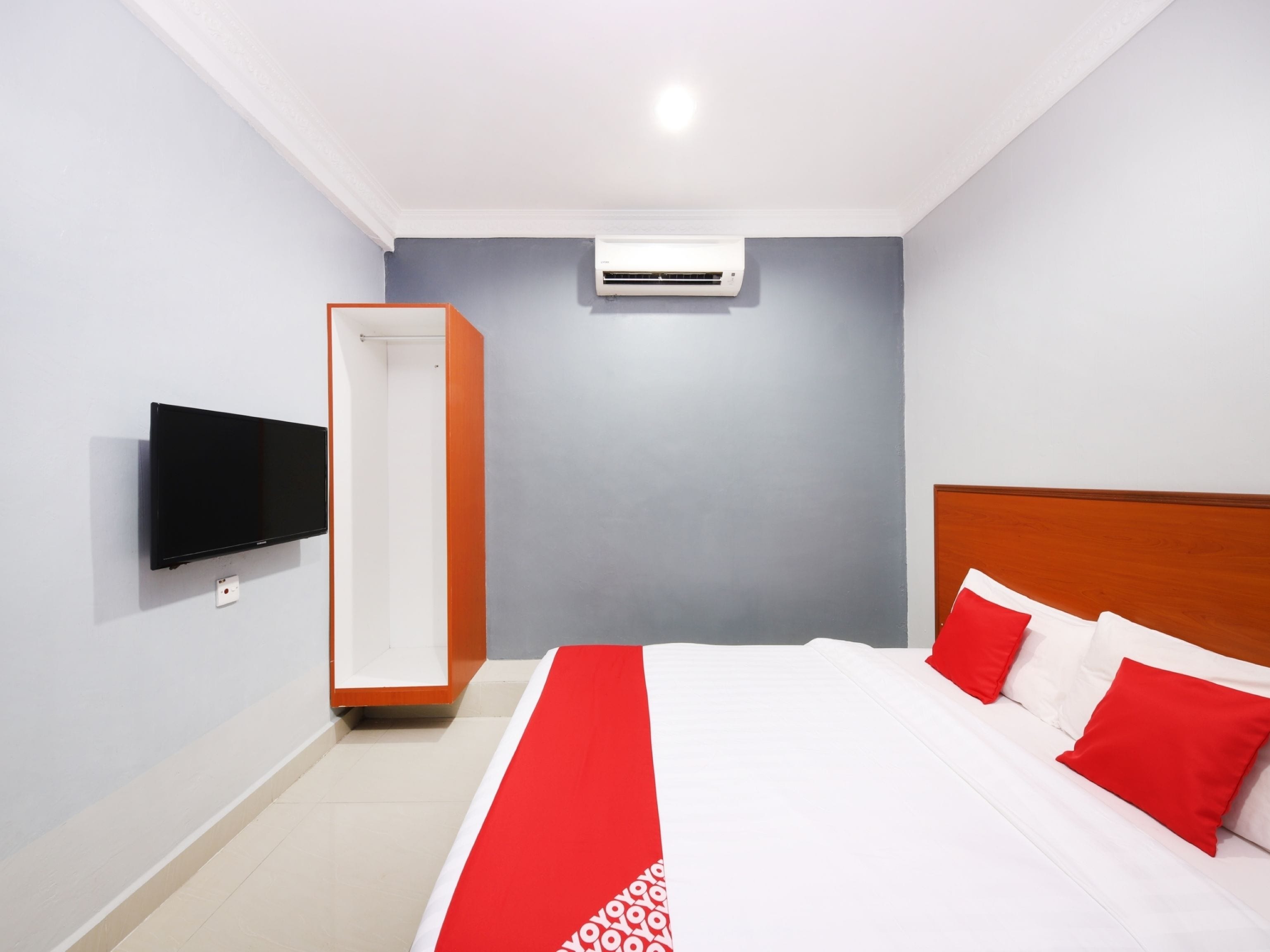 Quarto de hotel com cama, televisão fixada na parede e aparelho de ar condicionado.