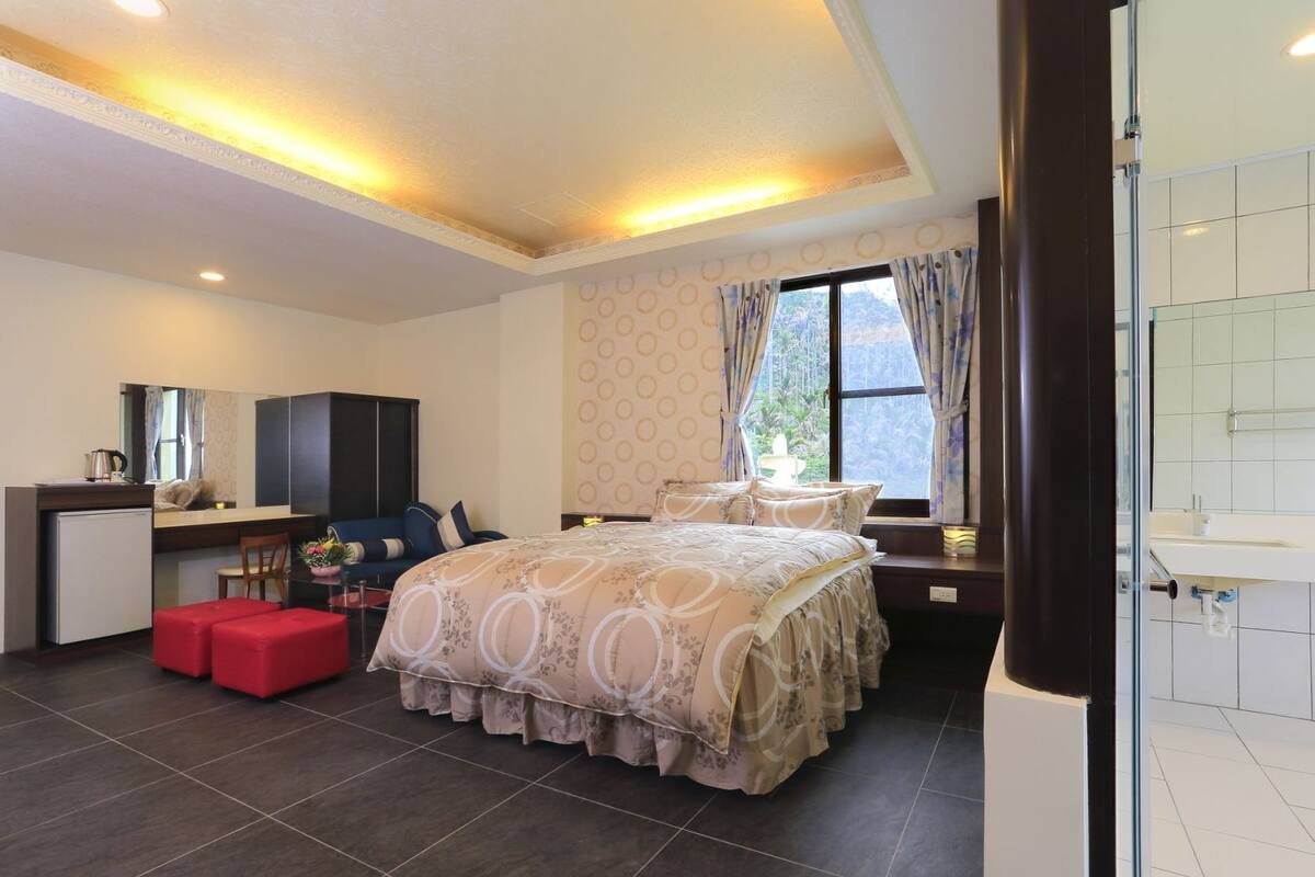 A modern bedroom with a bed, a desk, a chair, and a small kitchenette.