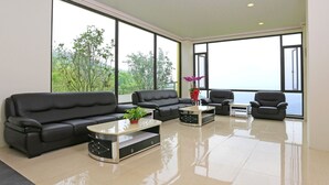 A spacious living room with a black leather sofa, a coffee table, and a chair. Large windows offer a view of greenery outside. - Tai An Cingjing (Zhushan)