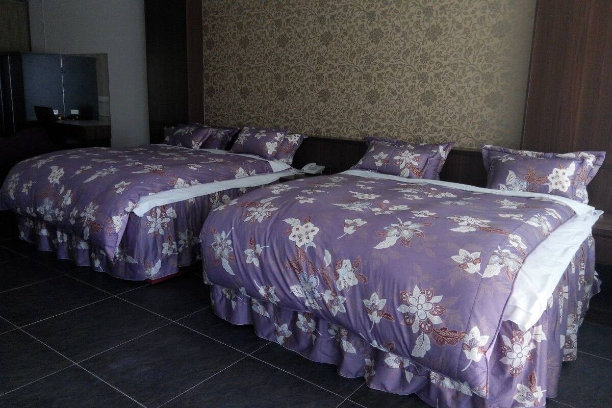 A hotel room with two beds, dark tiled flooring, a television, and a patterned wallpaper.