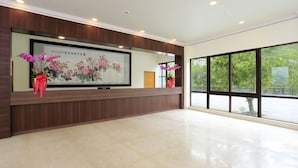 A reception area with a large framed artwork, wooden paneling, and two potted plants with pink flowers. - Tai An Cingjing (Zhushan)