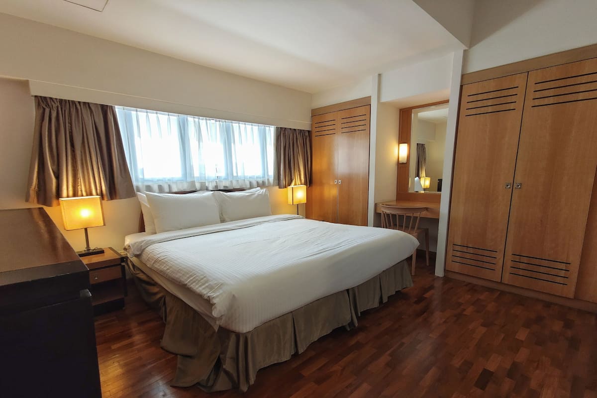 A hotel room with a large bed, wooden wardrobe, a desk with a chair, and a mirror.