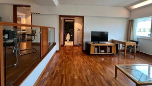 A modern living room with a wooden floor, a glass table, a TV, and a seating area.
