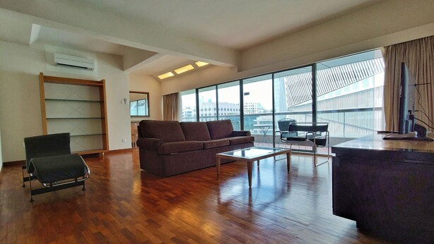 A spacious living room with a wooden floor, a sofa, a coffee table, and a balcony with a view of the city.