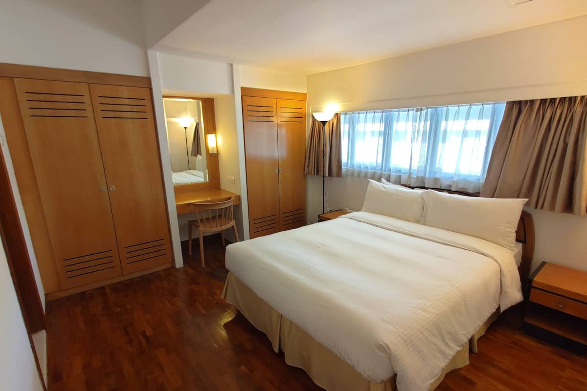 A bedroom with a large bed, wooden wardrobe, a desk with a chair, and a mirror.