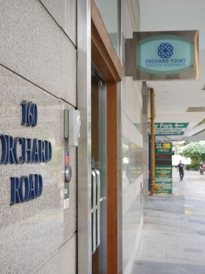 Entrada de un edificio con un cartel que dice "Orchard Point Serviced Apartments" y un cartel que indica "Car Park".