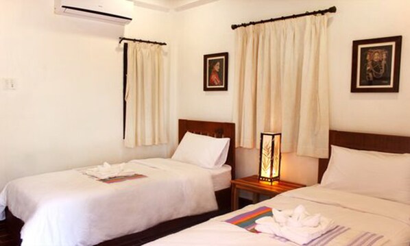 A hotel room with two single beds, a nightstand with a lamp, and a wall-mounted air conditioner.