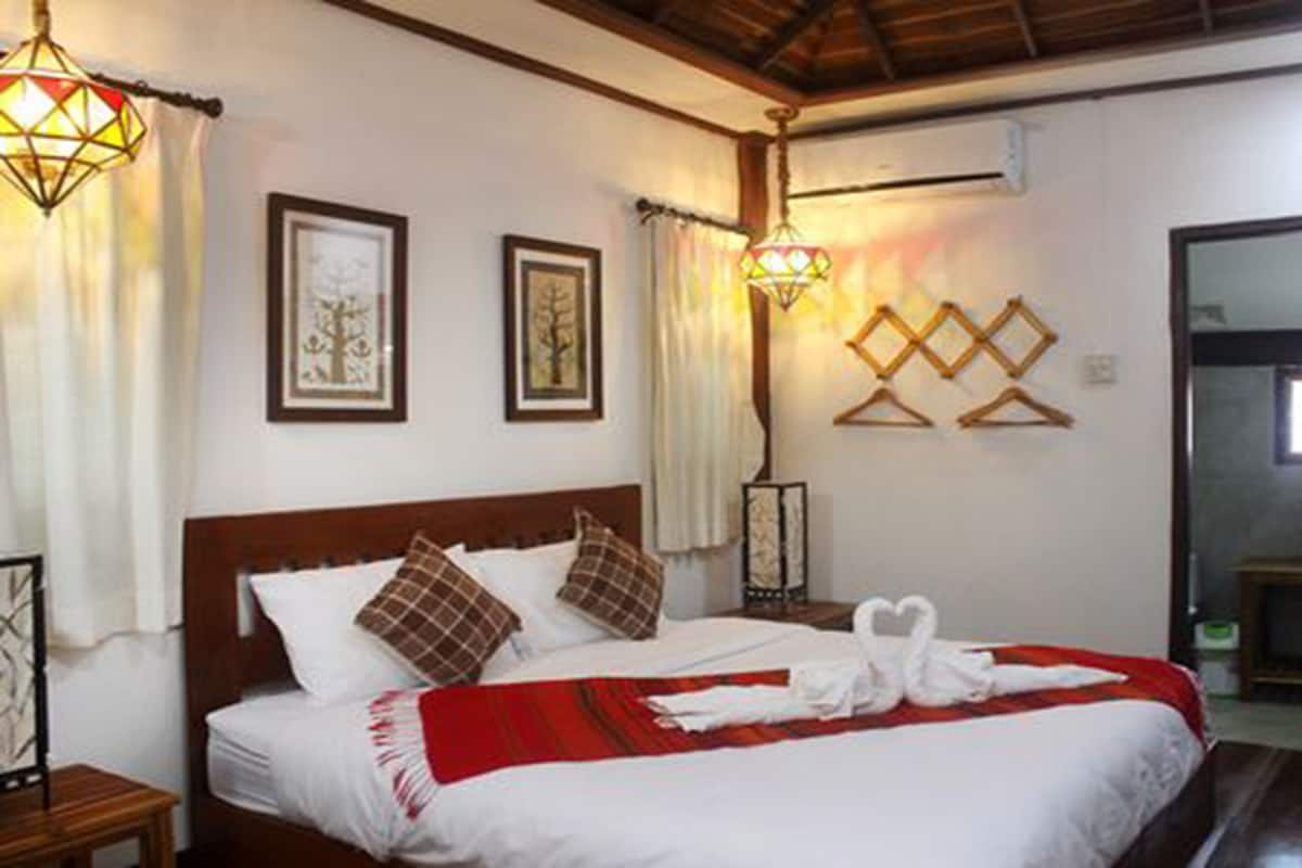 A neatly made bed with a red blanket, two framed pictures on the wall, and a hanging light fixture.