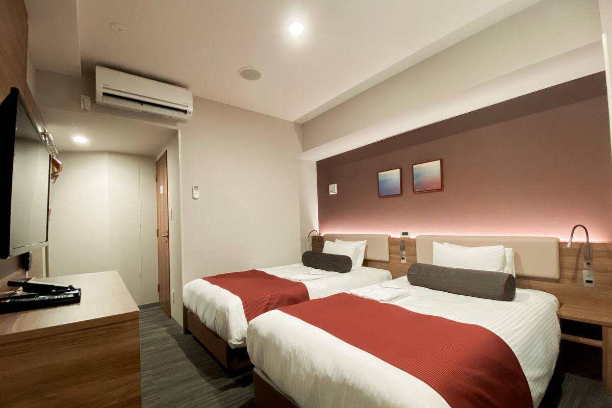A hotel room with two beds, a desk, and a TV.